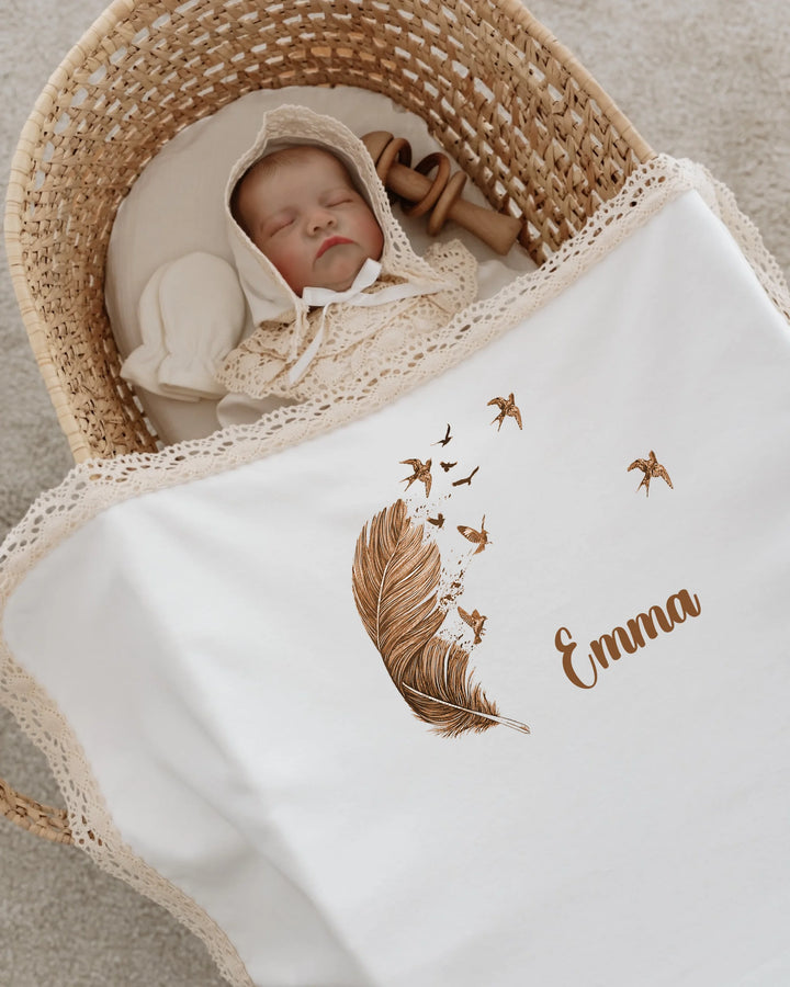 Newborn girl sleeping in a basket, wrapped in a personalized blanket with feather and bird design, name Emma.