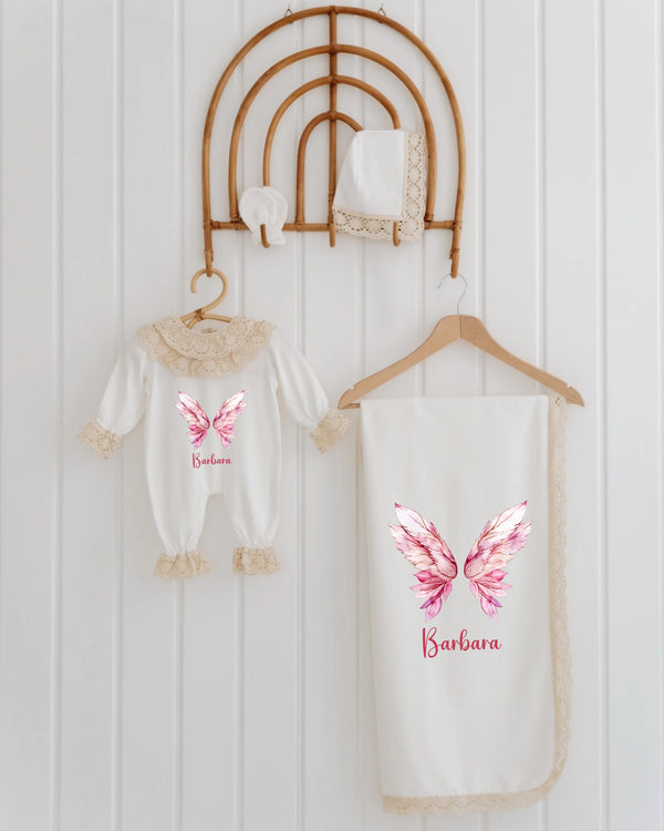 Gepersonaliseerde newborn set voor meisjes met vleugels, rompertje en dekentje met naam en kantdetails.